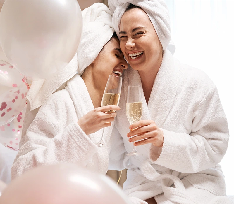 Two women in Cick white cotton bathrobes toasting with champagne